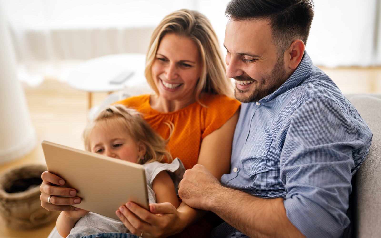 Une famille — deux parents et leur enfant — révise ensemble à la maison avec une tablette, dans une ambiance chaleureuse